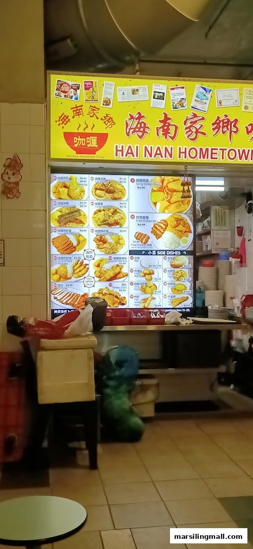 A brightly lit menu board displaying various Hainanese curry dishes and side orders with prices.