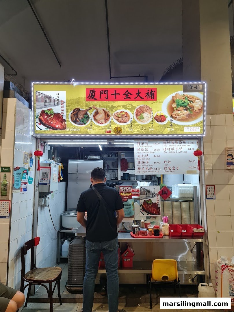 A person stands in front of the 'Herbal Soup Pig Trotter' stall with its illuminated menu board.