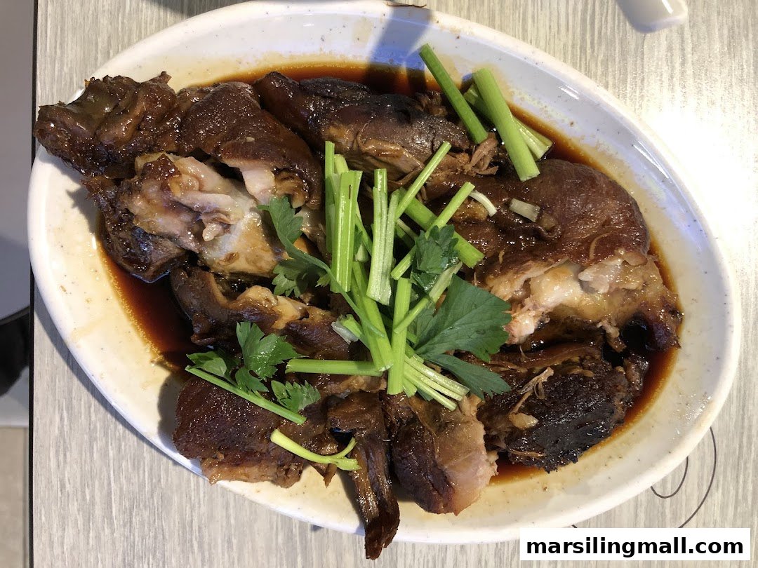 A plate of braised pig trotters with dark sauce and green garnishes.