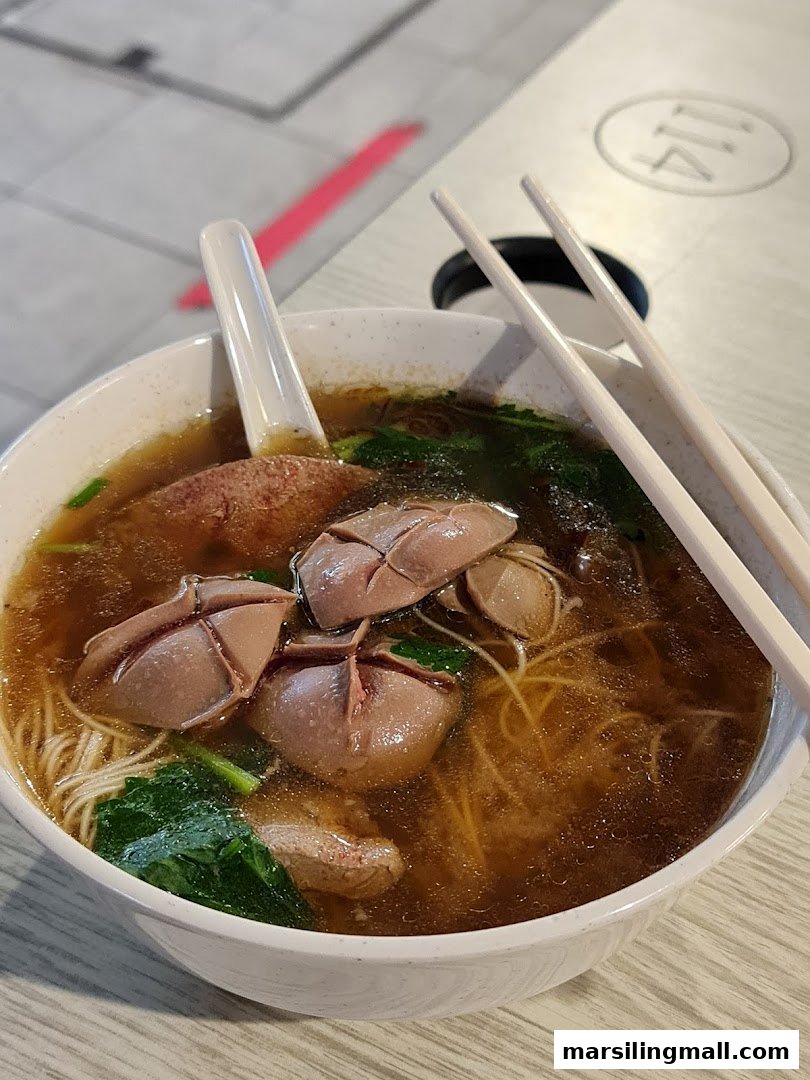 A close-up of a bowl of traditional herbal soup noodles with pig offal and greens.