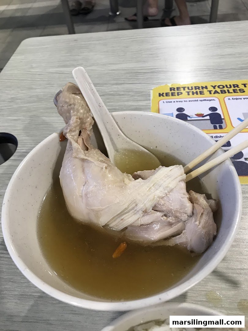 A close-up of a bowl of traditional herbal chicken soup with a large chicken drumstick.