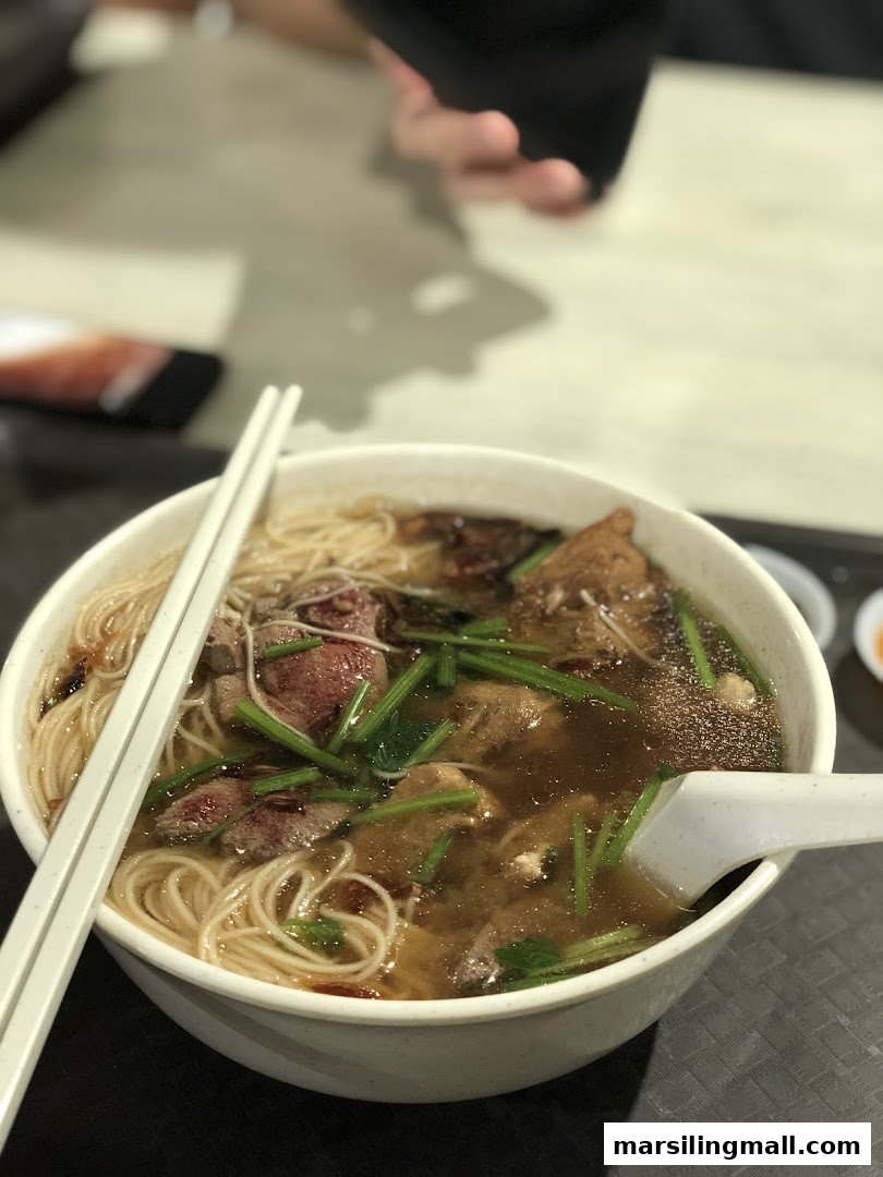 A close-up of a hearty bowl of herbal soup noodles with various meats and greens.