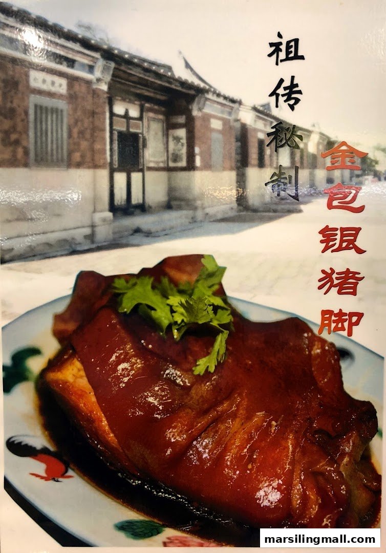 A close-up of a braised pig trotter dish with cilantro, against a traditional Chinese building backdrop.