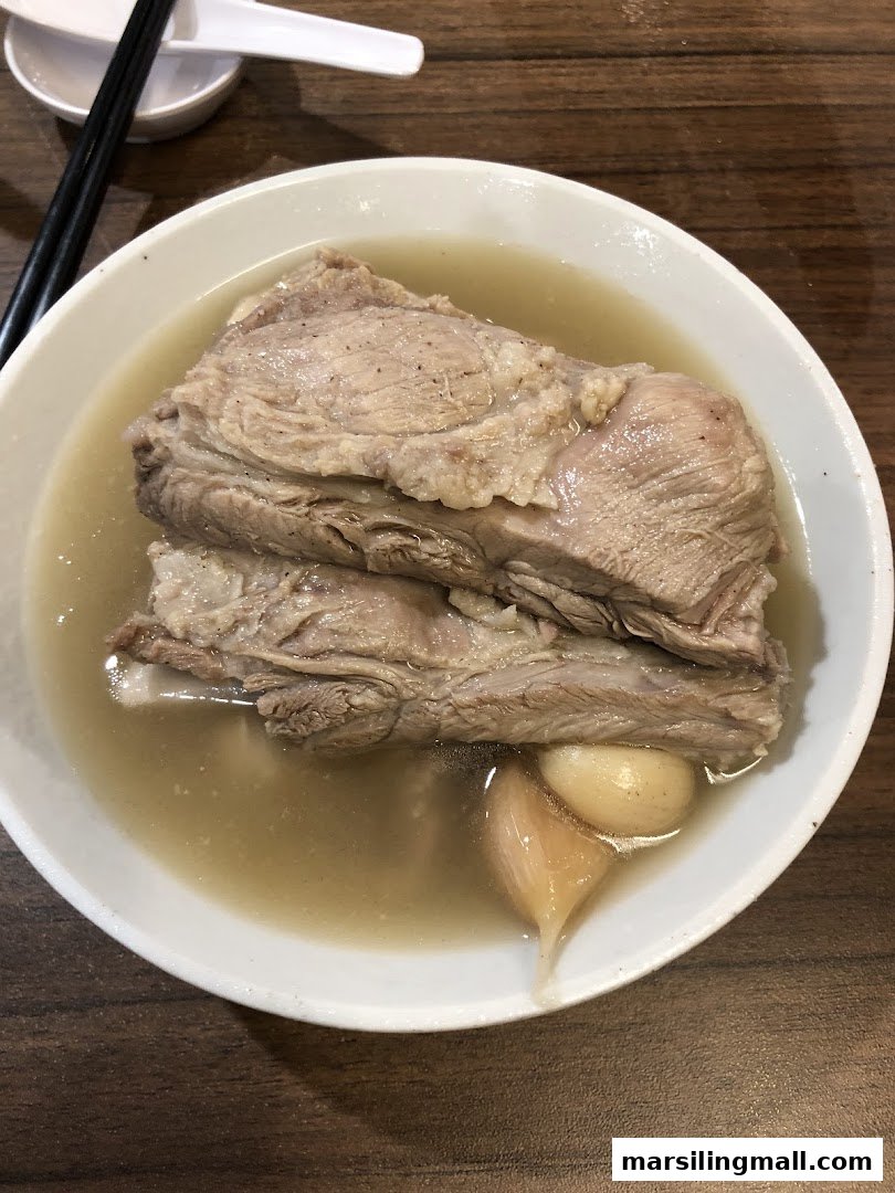 A close-up of a bowl of tender pork ribs in a savory herbal soup with garlic cloves.