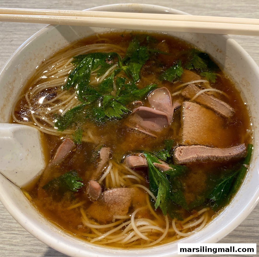 A close-up of a bowl of savory noodles with meat slices and green herbs in a rich broth.