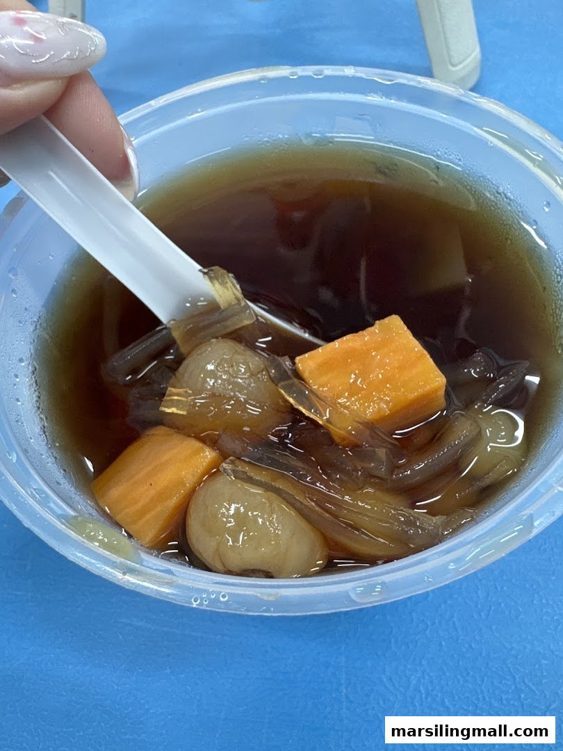 A close-up of a traditional dessert with sweet potato, longan, and jelly in a clear bowl.