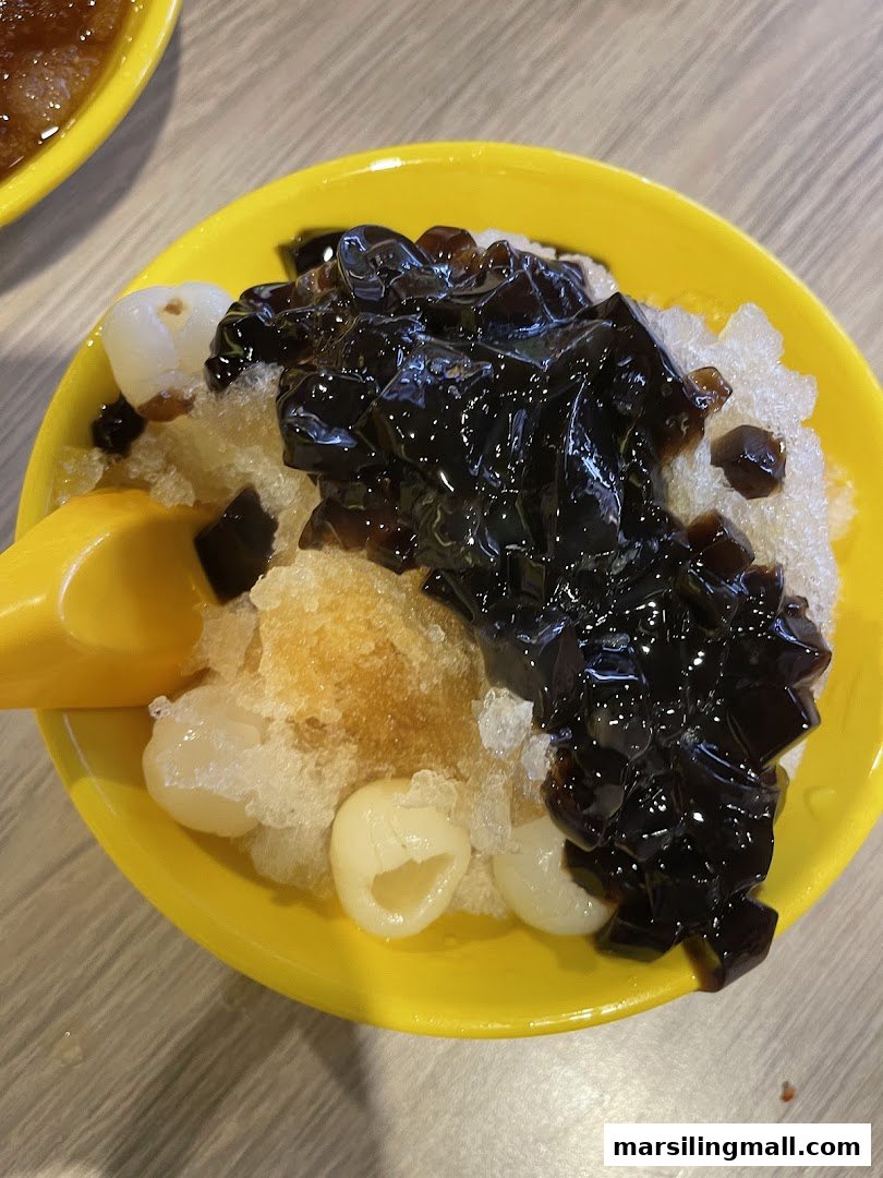 A vibrant yellow bowl filled with shaved ice, grass jelly, and longans, a refreshing dessert.