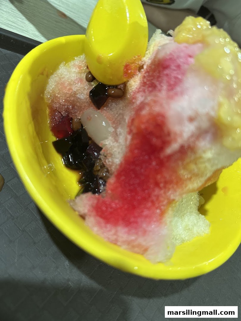 A vibrant bowl of shaved ice dessert with colorful syrups and various toppings in a yellow bowl.