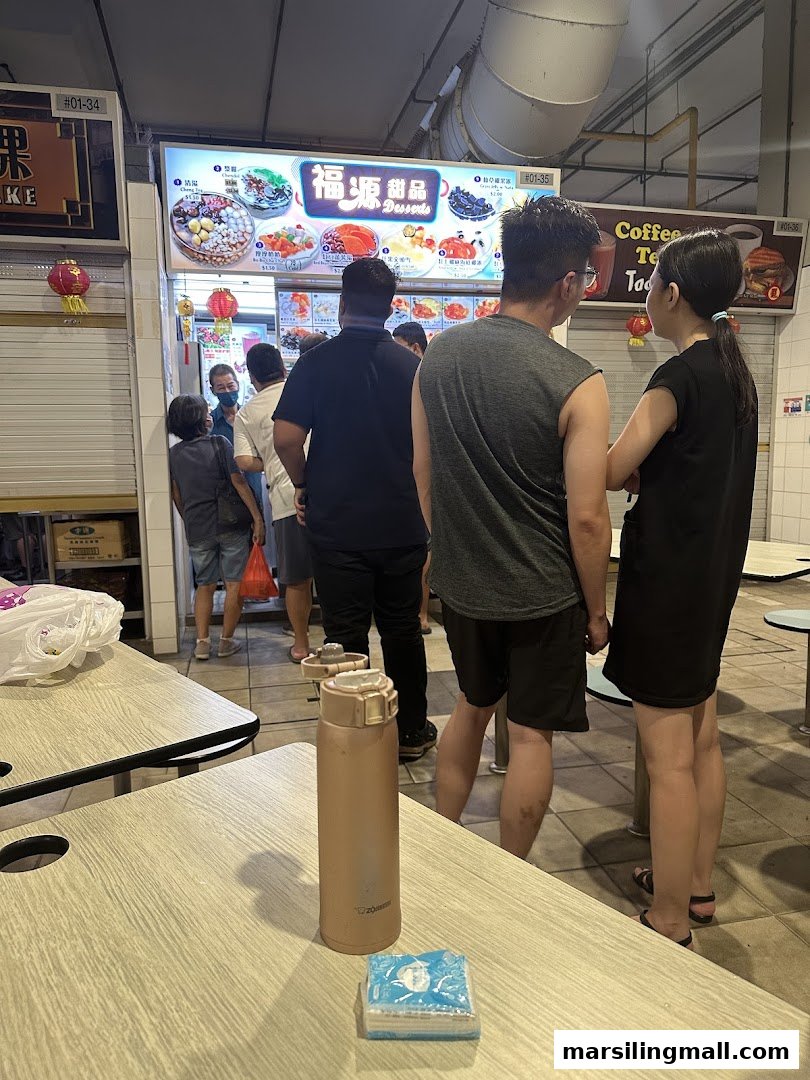 Customers queueing at the brightly lit Hock Guan Desserts stall, showcasing various sweet treats.