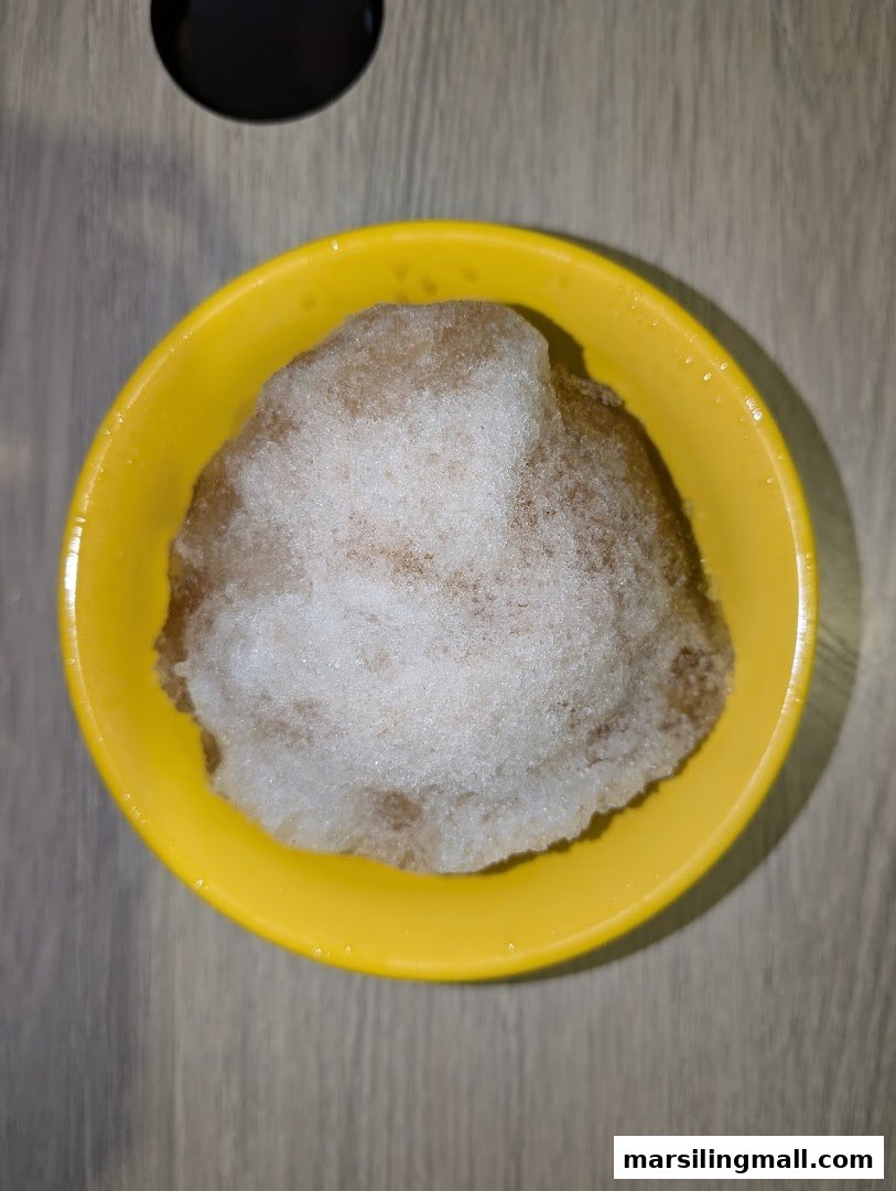 A yellow bowl filled with a brown shaved ice dessert topped with white ice.