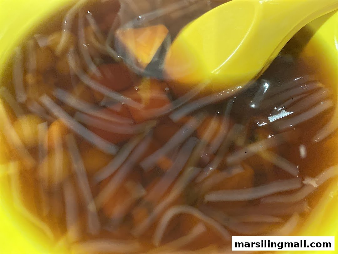 A close-up of a refreshing dessert with clear noodles and orange pieces in a vibrant yellow bowl.