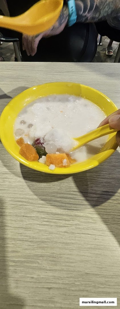 A vibrant yellow bowl of traditional Asian dessert with shaved ice, sweet potato, and pearls, being enjoyed with a spoon.
