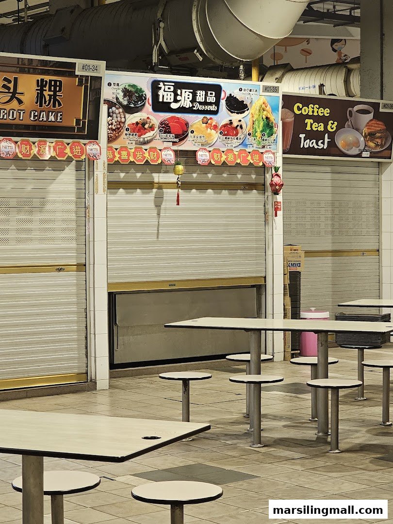 The closed stall front of Hock Guan Desserts, featuring its vibrant menu board and nearby food court seating.