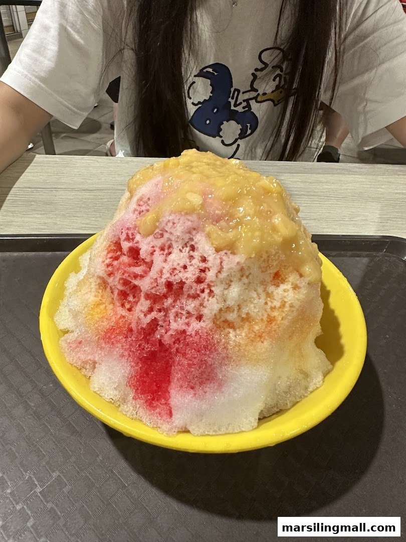 A vibrant, colorful shaved ice dessert with fruit topping in a yellow bowl, served on a tray.