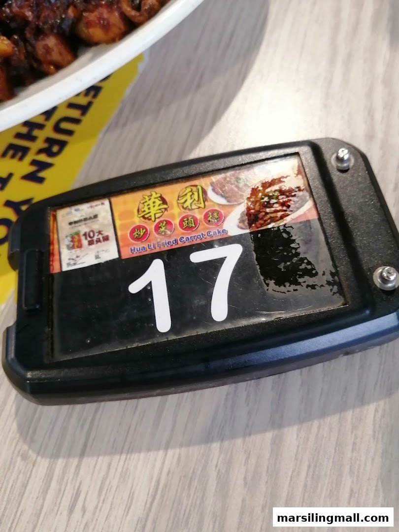 A close-up of a table number/buzzer for Hua Li Fried Carrot Cake, featuring food images.