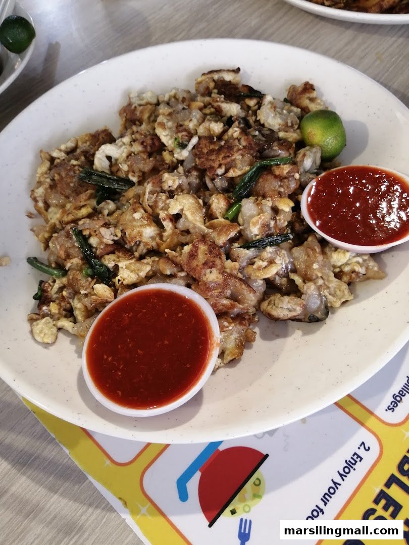 A plate of savory fried carrot cake with two servings of chili sauce and a lime wedge.
