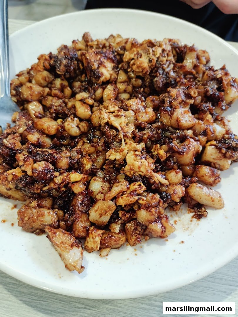 A close-up of a plate of dark fried carrot cake with visible egg and radish cake pieces.