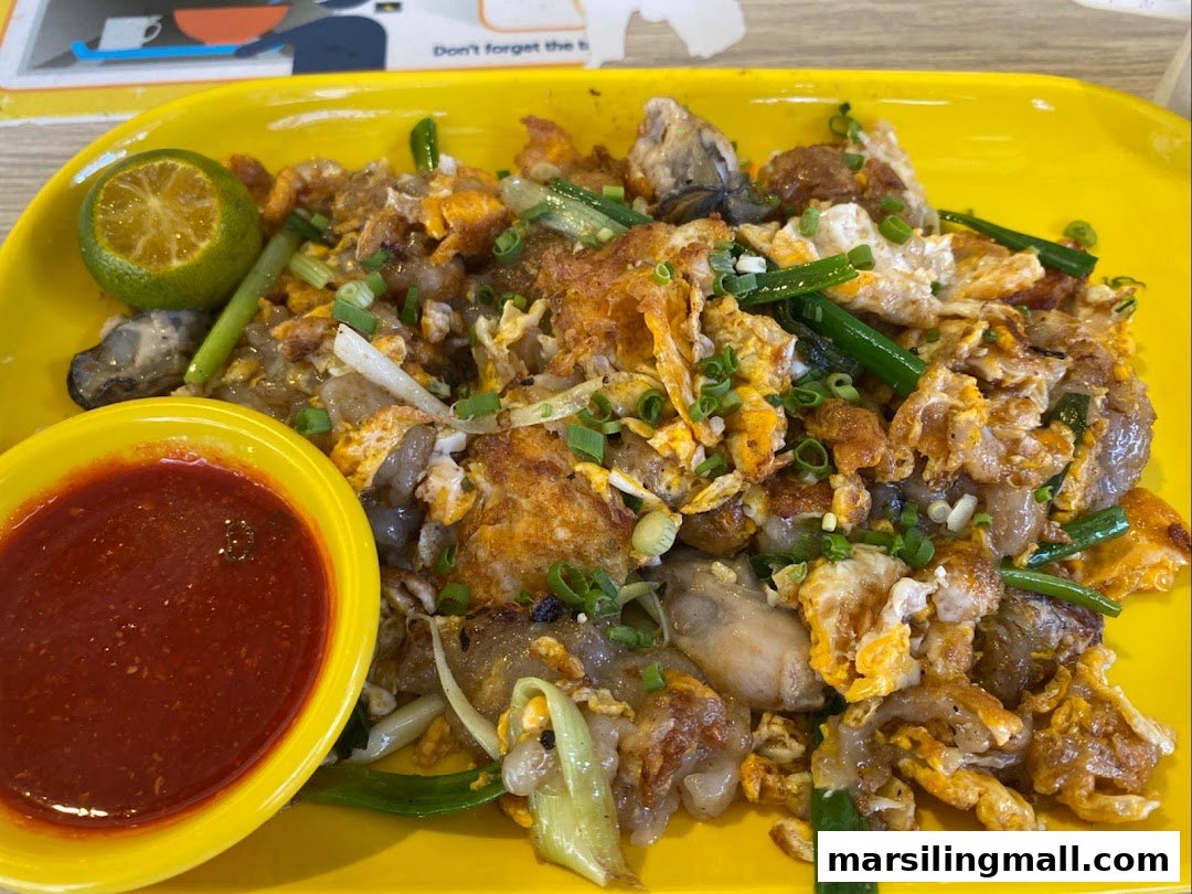 Close-up of fried carrot cake with egg, oysters, spring onions, chili sauce, and lime.