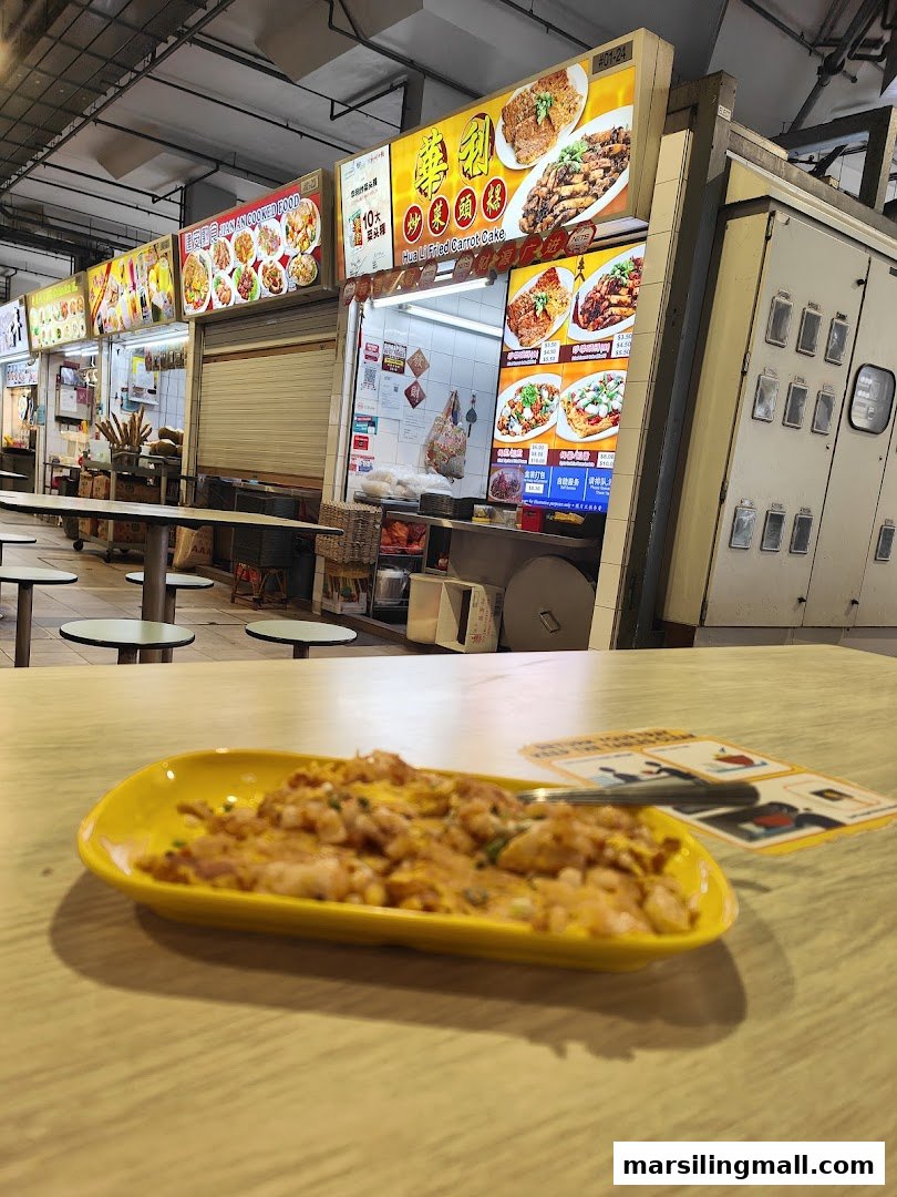 A plate of fried carrot cake on a table with the Hua Li Fried Carrot Cake hawker stall in the background.