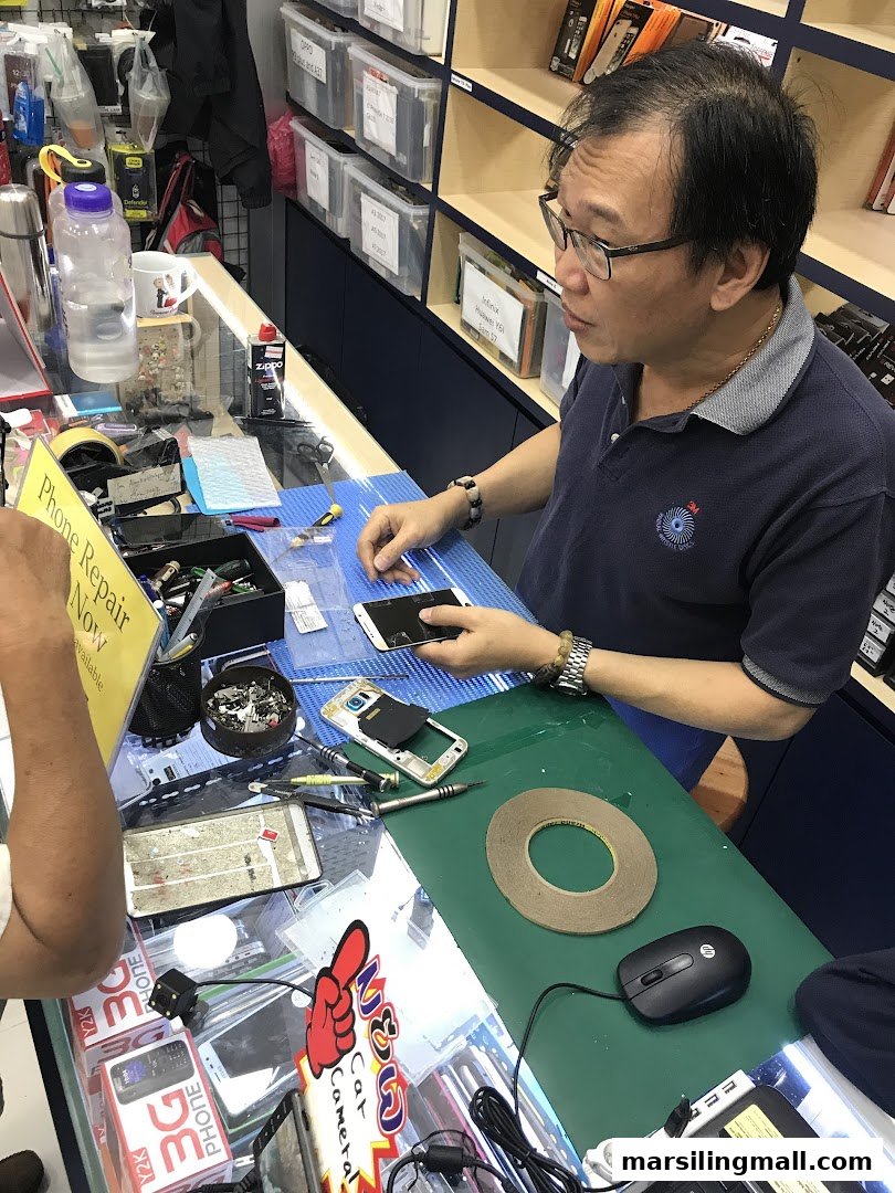 A technician at ImobileHub meticulously repairs a smartphone at a busy counter, surrounded by tools and parts.
