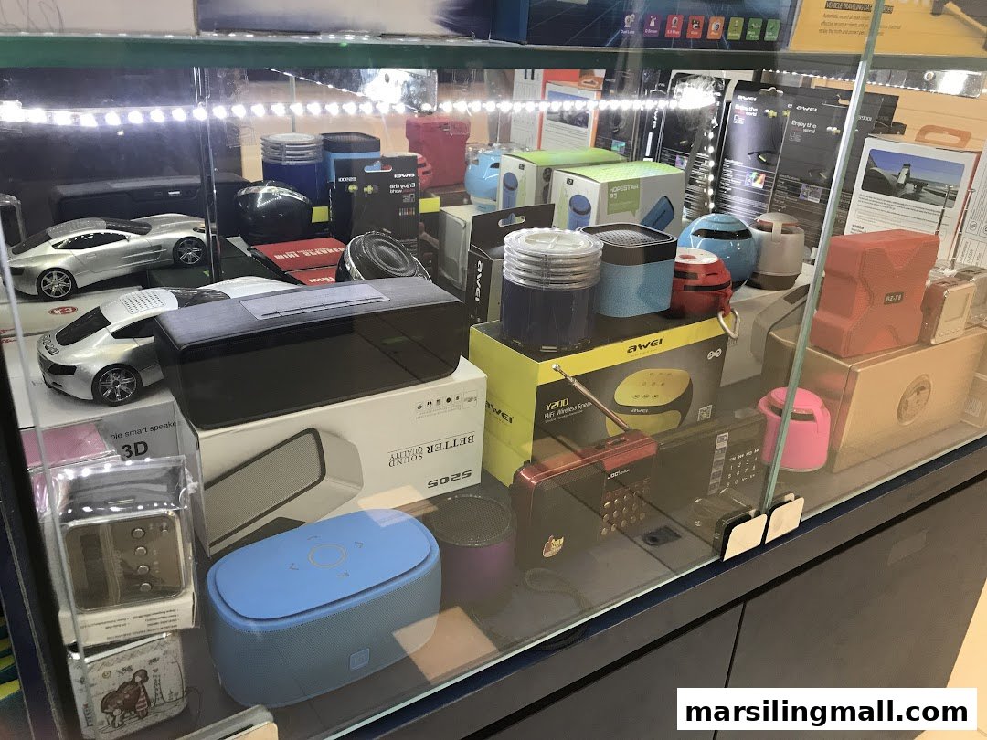 A brightly lit display case showcasing a variety of portable speakers and electronic gadgets.