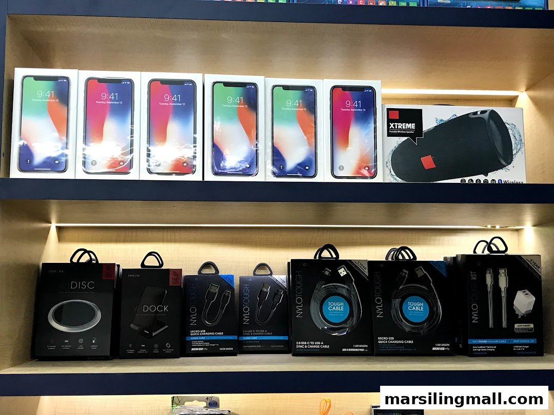 A display of mobile phones, wireless speakers, and various charging accessories on shop shelves.