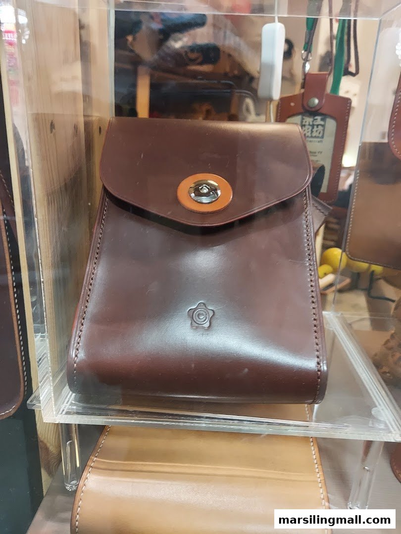 A dark brown leather bag with a unique clasp and embossed logo, displayed in a clear case.