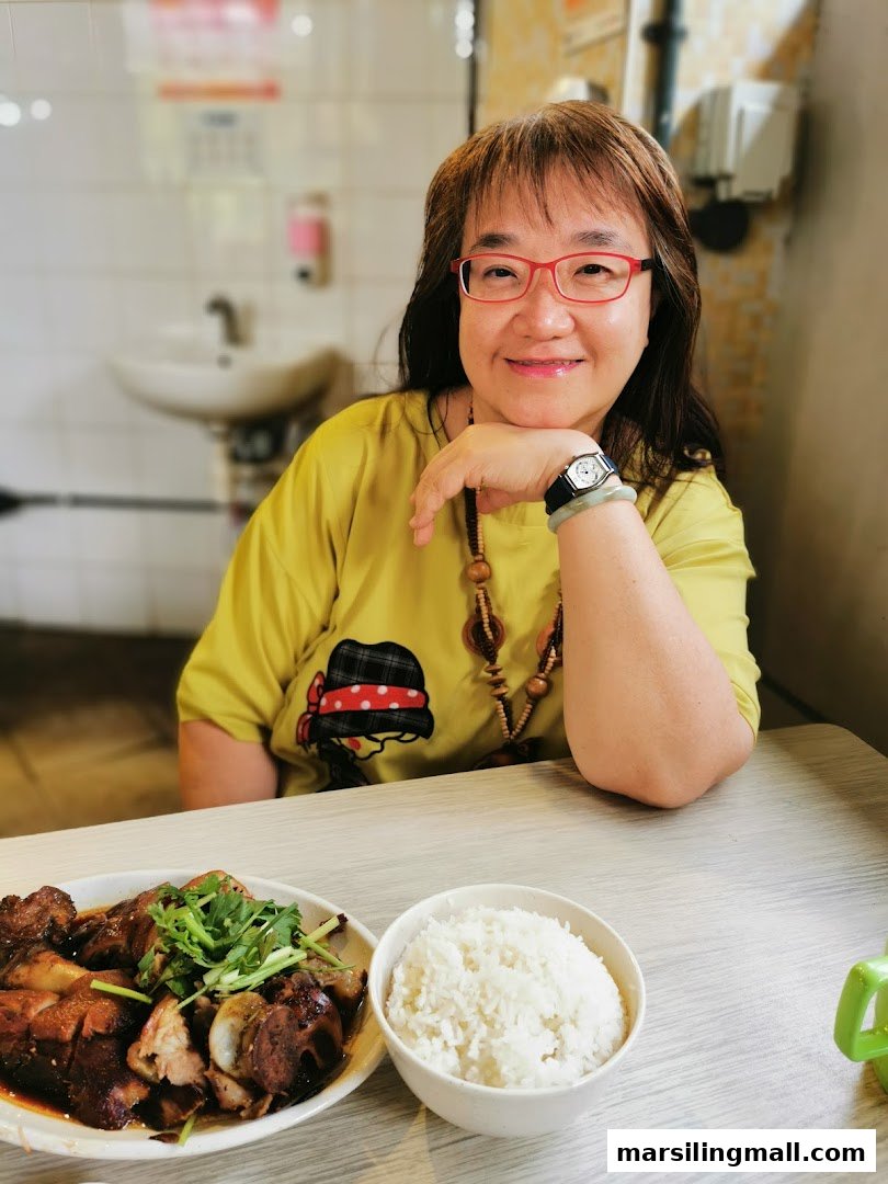 A smiling woman enjoys a meal of cooked meat and rice at Jian An Cooked Food.
