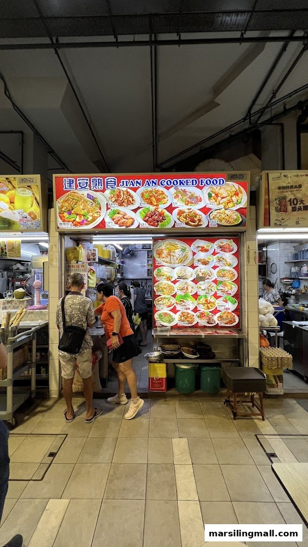 Front view of Jian An Cooked Food stall with customers and vibrant food display boards.