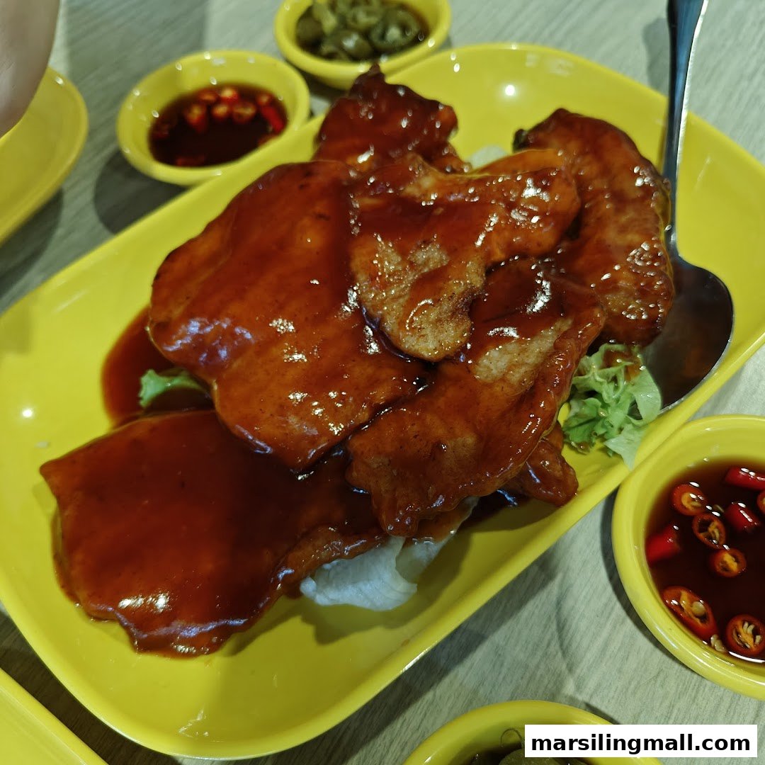 A vibrant yellow plate holds saucy, tender pork cutlets, accompanied by chili and pickled condiments.