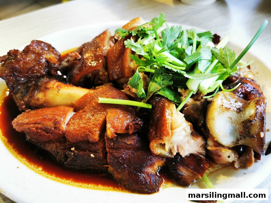 A close-up of a plate of braised pork or trotters, garnished with fresh green herbs and rich sauce.