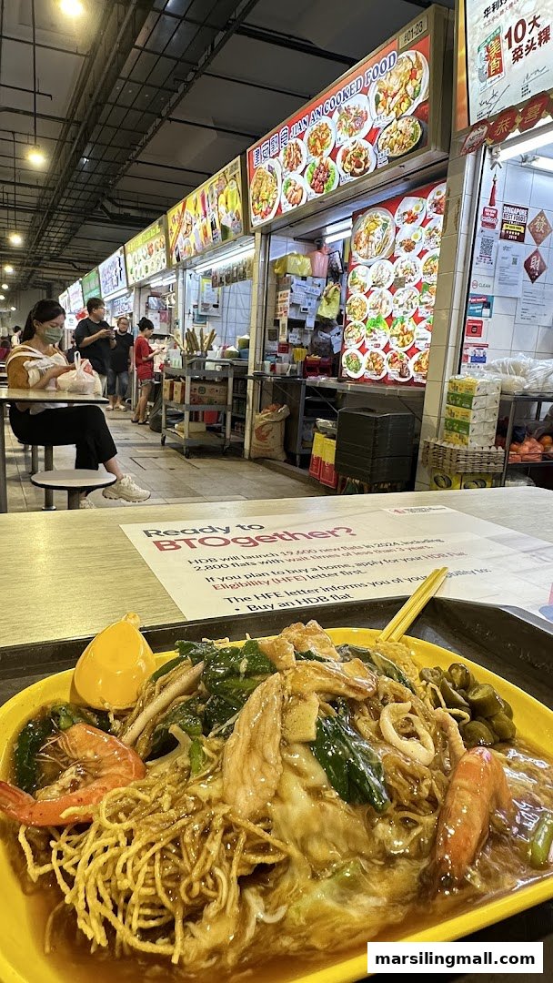 A delicious plate of seafood noodles in the foreground, with the 'Jian An Cooked Food' stall visible in a bustling hawker centre.