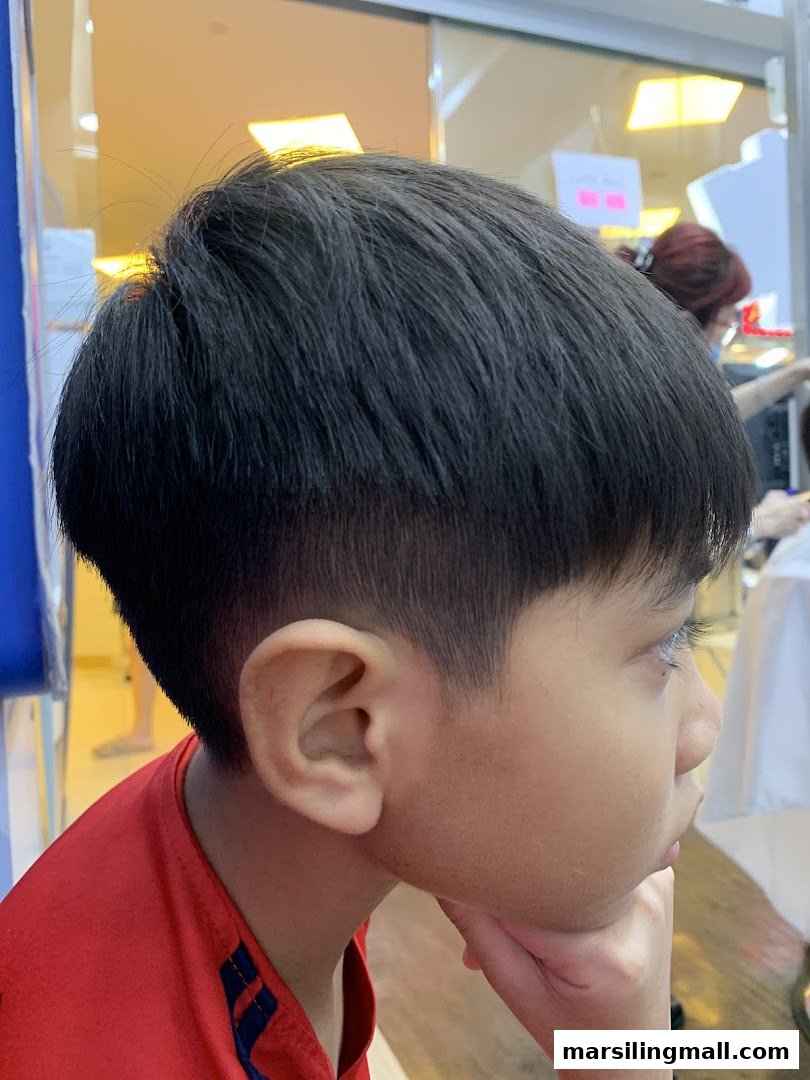 A young person with a fresh haircut, seen from the side, inside a salon.