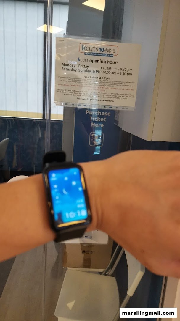 A kcuts sign displays opening hours and a ticket machine, partially obscured by a wrist.