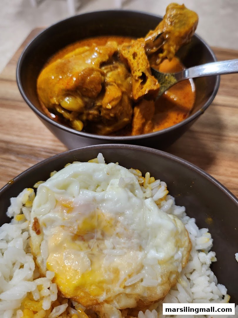 A close-up of a rich chicken curry and a bowl of rice topped with a fried egg.