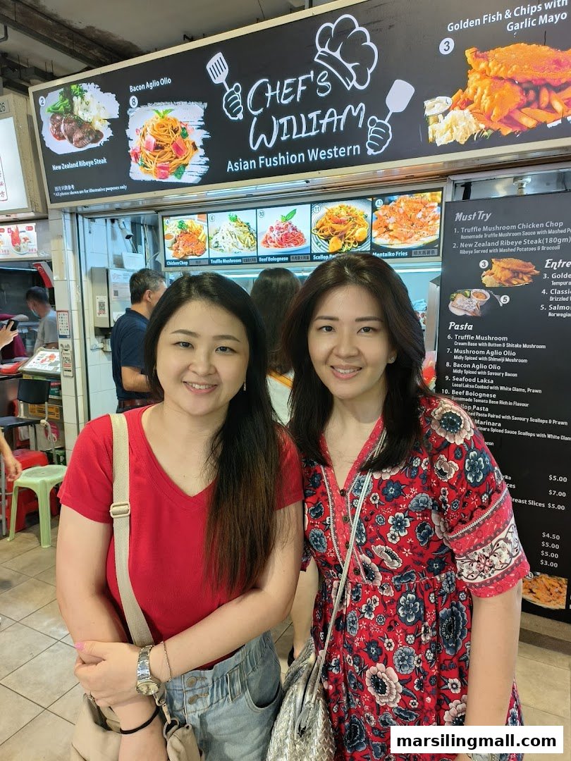 Two women smiling in front of the 'Chef's William' Asian Fusion Western food stall.