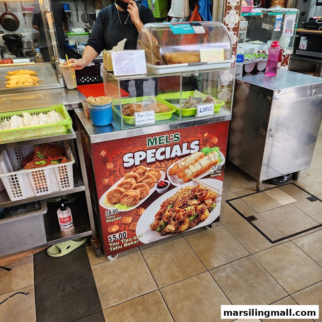 A hawker stall displaying "Mel's Specials" menu board with various fried snacks and traditional delights.