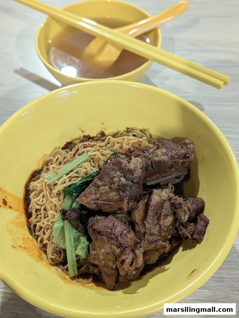 A vibrant yellow bowl of saucy noodles with braised meat and greens, accompanied by a soup.
