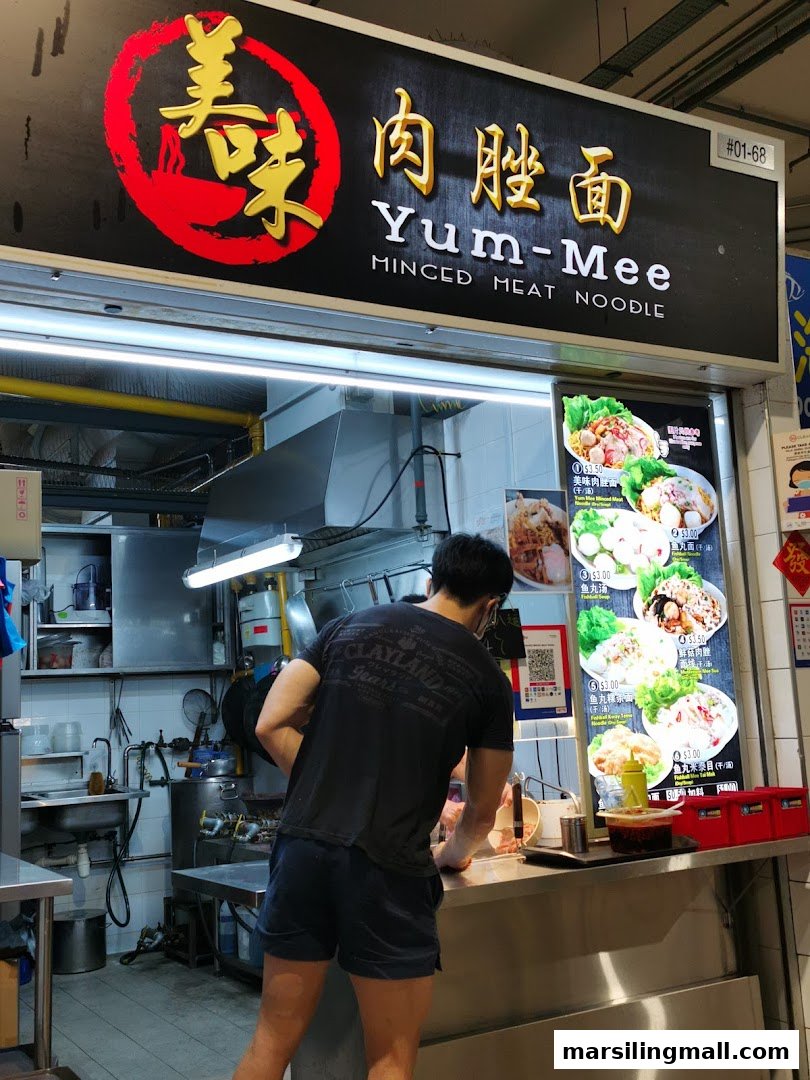 A hawker stall named Yum-Mee Minced Meat Noodle with a staff member preparing food.