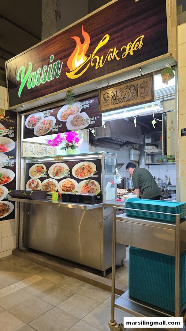 A bustling hawker stall, Yassin Wok Hei, with a chef preparing food and display boards showcasing dishes.