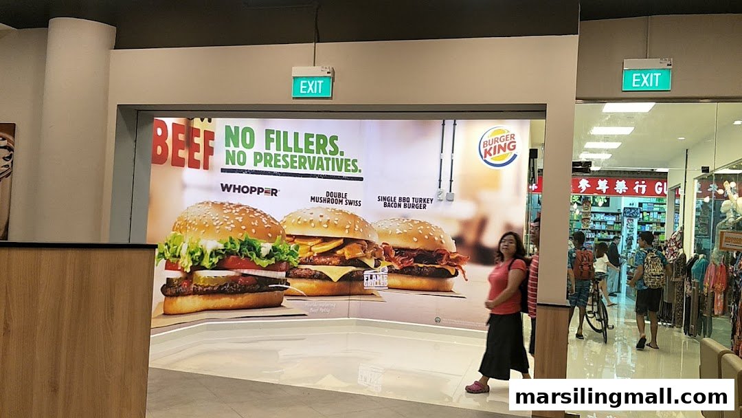 The entrance of a Burger King outlet featuring a large advertisement for its flame-grilled burgers.