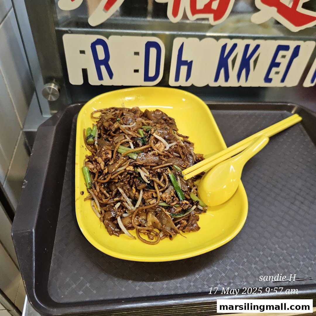 A plate of delicious Char Kway Teow with yellow utensils on a black tray.