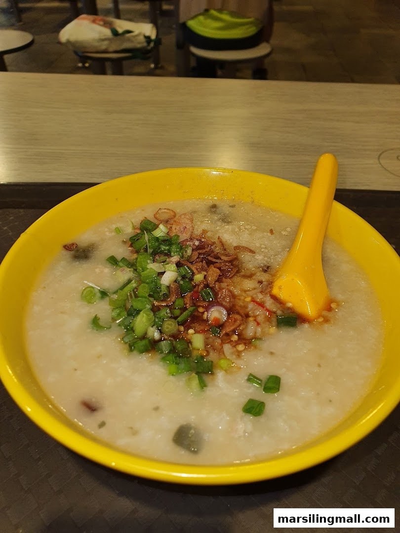 A vibrant yellow bowl of congee topped with spring onions, fried shallots, and chili oil.
