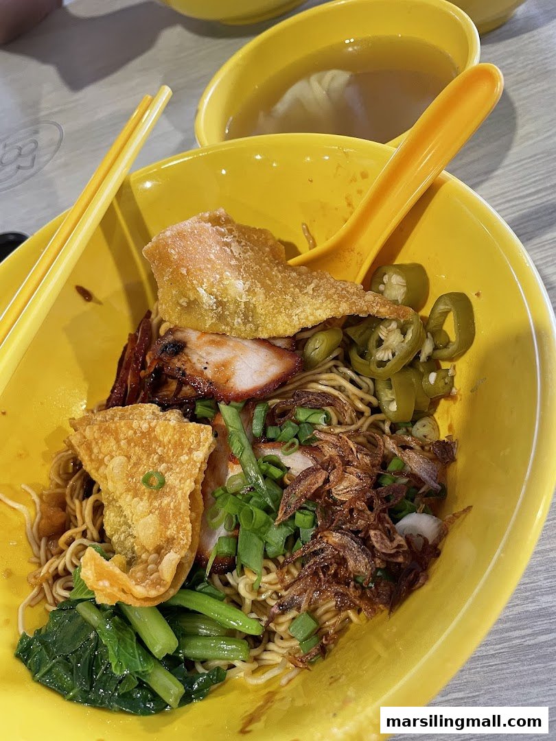A vibrant yellow bowl of delicious wanton mee with char siew, fried wontons, and fresh greens.
