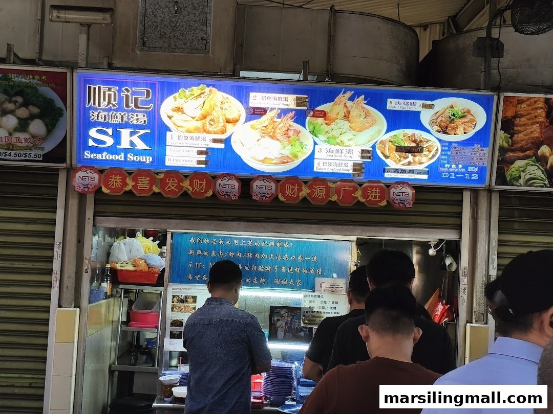 A bustling hawker stall, SK Seafood Soup, with a vibrant menu board and customers queuing.