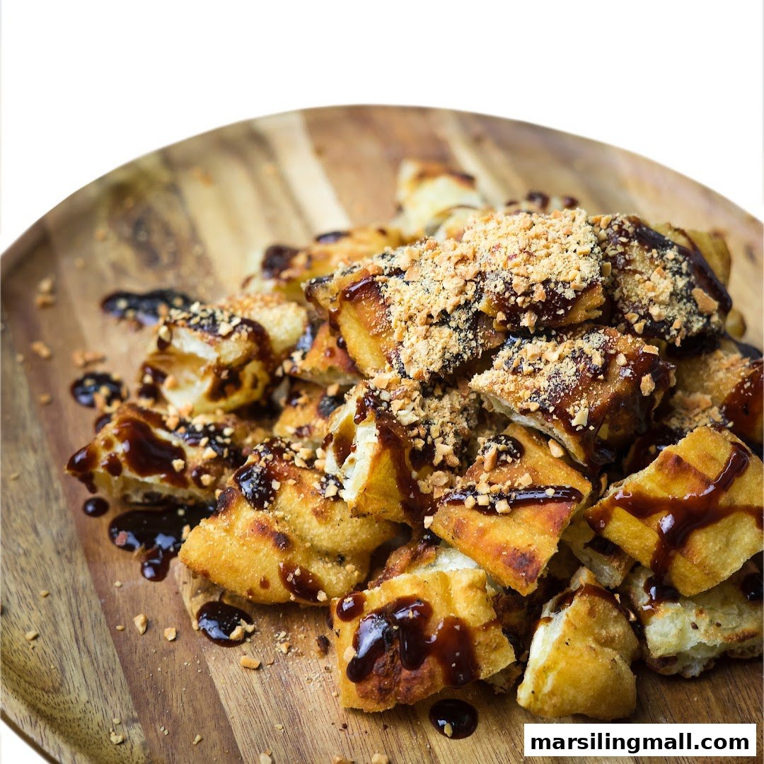 A wooden plate filled with golden-brown fried dough fritters drizzled with dark sauce and crushed peanuts.