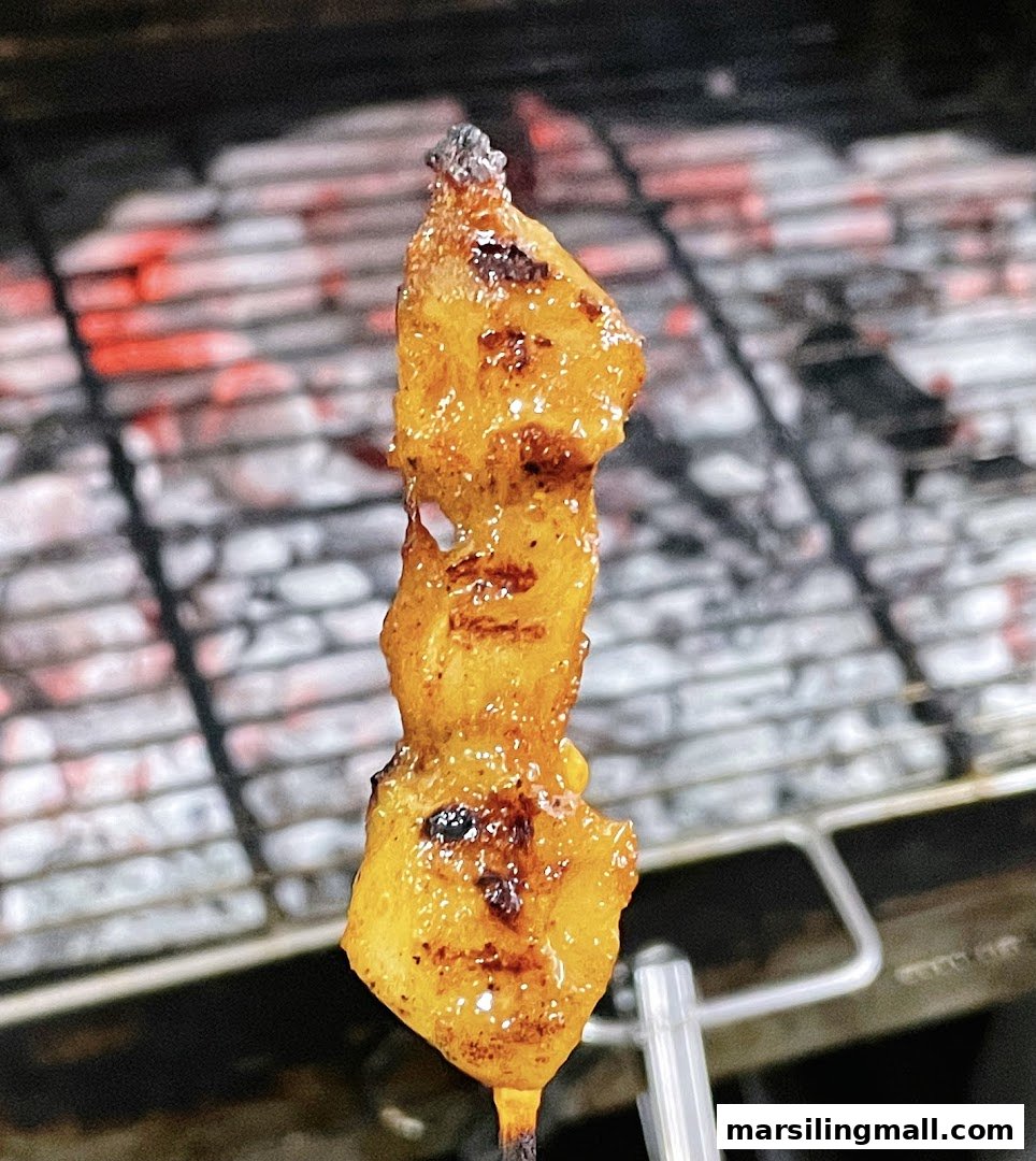 A close-up of a delicious satay skewer grilling over hot coals, showing its glazed texture.
