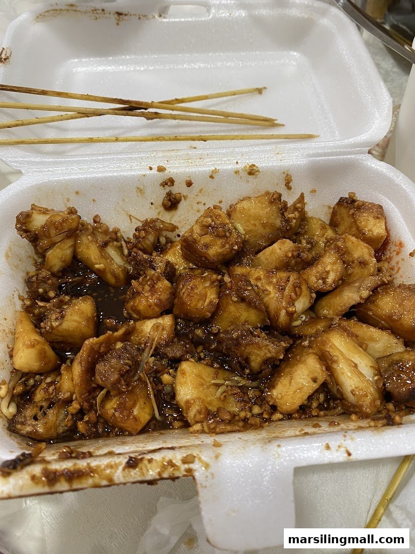 A close-up of a takeaway box filled with delicious Rojak, featuring a rich sauce and various ingredients.