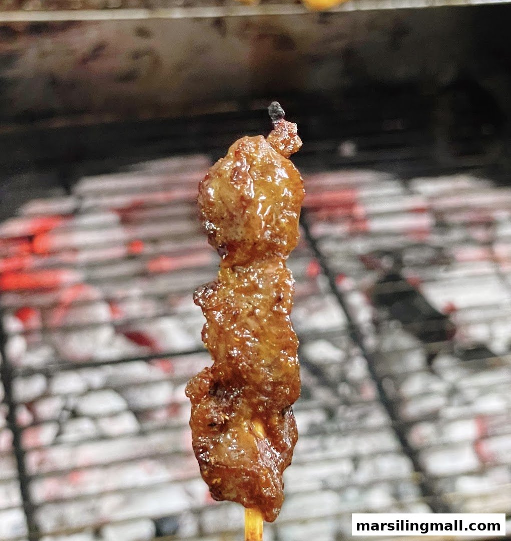 A close-up of a glistening satay stick grilling over hot coals.