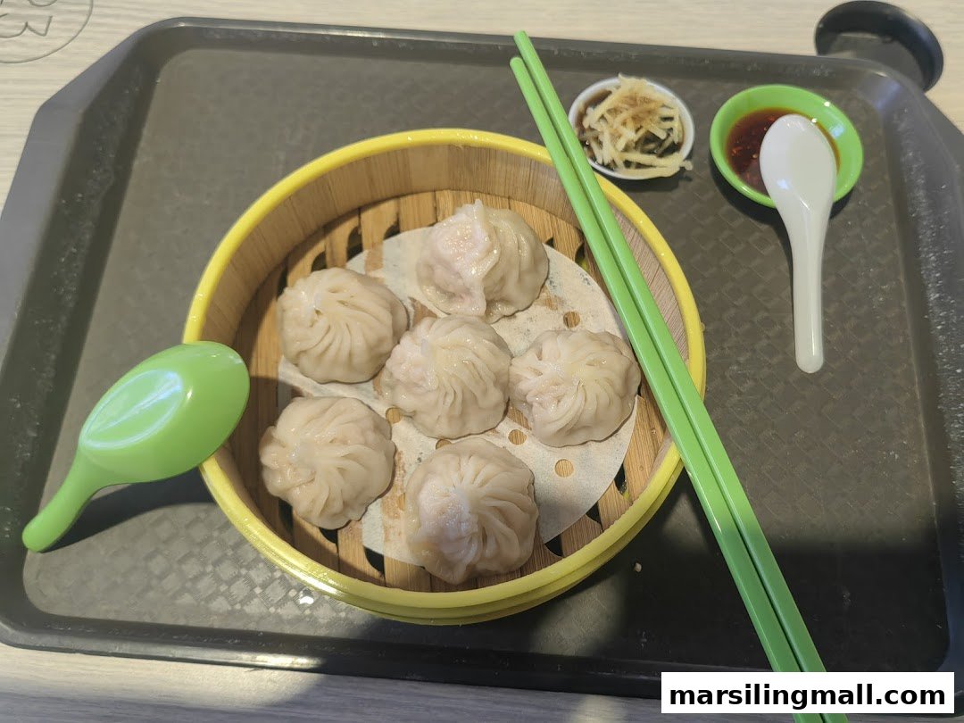 A bamboo steamer filled with delicious xiao long bao, accompanied by chopsticks and dipping sauces on a tray.